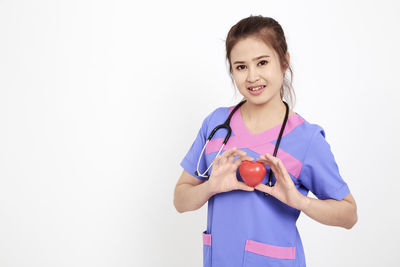 Portrait of female doctor with heart model standing against white background