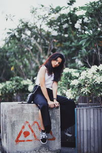 Portrait of young woman sitting on plant against trees