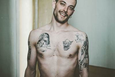 Portrait of shirtless man with tattoo standing at home