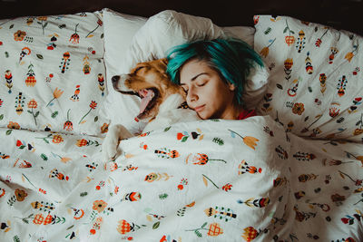 High angle view of woman sleeping with dog on bed