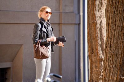 Young woman holding pouch while standing by building