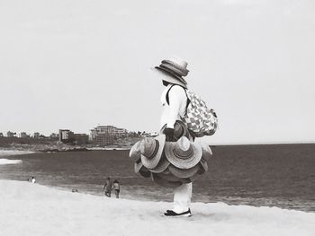Man selling hats while standing on sand at beach