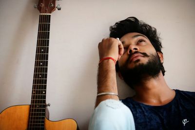 Close-up of thoughtful man sitting with guitar against wall