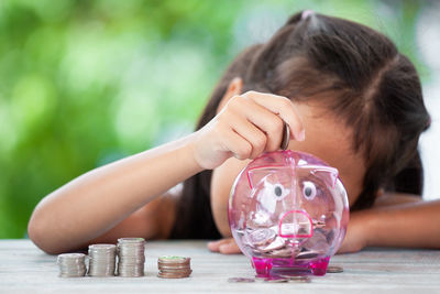 Girl putting coin in piggy bank at table