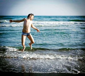 Full length of shirtless boy jumping on beach