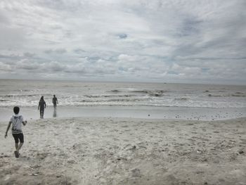 Rear view of people walking on beach against sky