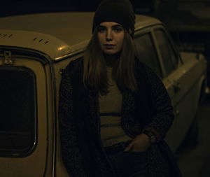 Portrait of young woman leaning on car at night