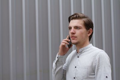 Young man standing against wall talking on mobile phone