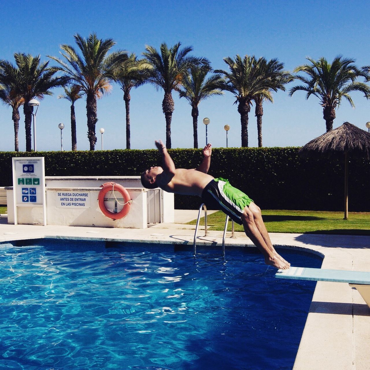 MAN JUMPING AT SWIMMING POOL AGAINST SKY