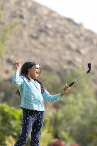 Side view of woman with arms raised standing outdoors