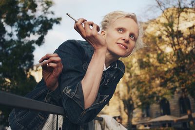 Mid adult woman holding cigarette while leaning on railing 
