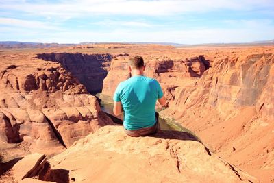 Rear view of man sitting on horseshoe bend edge