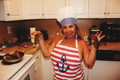 Portrait of woman holding raw seafood while standing in kitchen