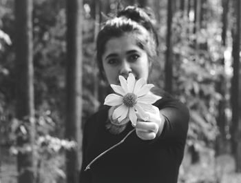 Portrait of young woman holding flower while standing in forest