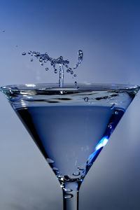 Close-up of water splashing on glass against blue background