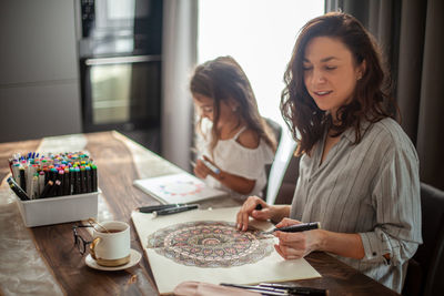 Smiling mother and daughter drawing at home