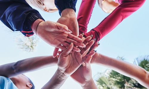 From below team of crop anonymous diverse female athletes stacking hands while standing against cloudless blue sky on sunny day