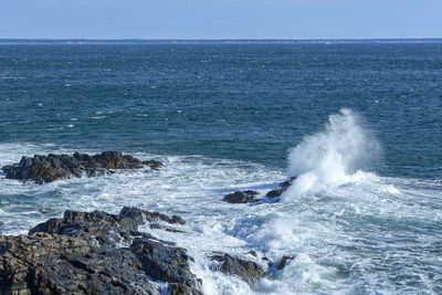 Waves splashing on rocks against blue sky