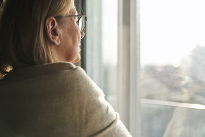 Side view of young woman looking through window