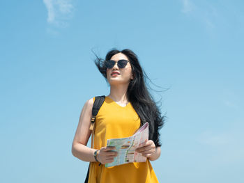 Low angle view of young woman wearing sunglasses standing against sky