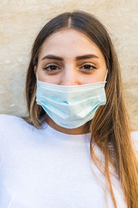 Portrait of beautiful young woman wearing mask against wall outdoors