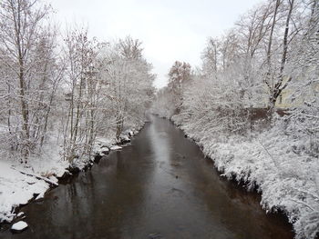 Snow covered plants by canal against sky