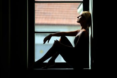 Side view of woman sitting on window