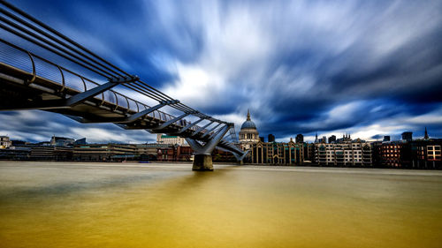 Bridge over river by buildings against sky