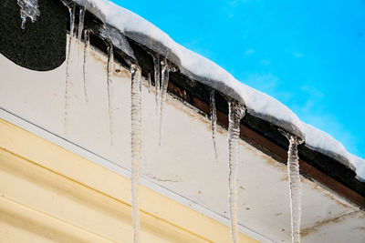 Icicles on snow covered metal against blue sky