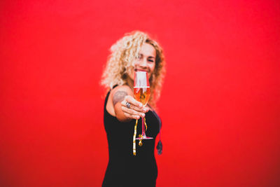 Portrait of a young woman drinking glass against red background