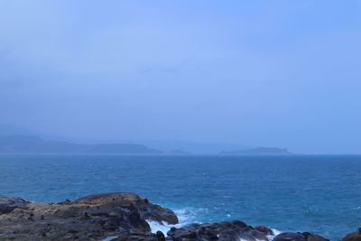 Scenic view of blue sea against gloomy sky