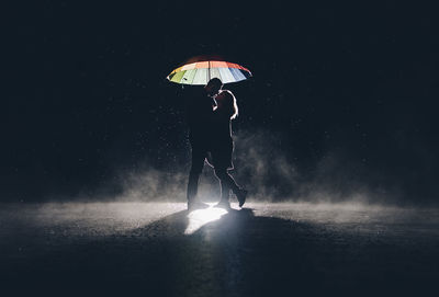 Couple with umbrella standing against sky at night