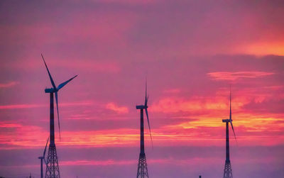 Low angle view of silhouette cranes against dramatic sky during sunset