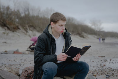 Teenager sits on the beach reads a book, looks into a textbook. immersed in the study of the materia