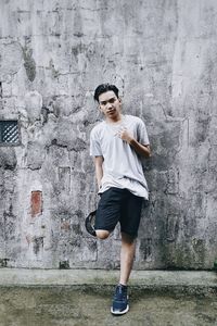 Full length portrait of young man leaning against wall