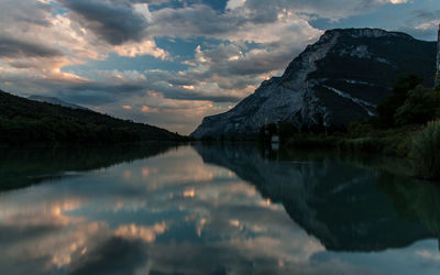 Scenic view of calm lake with mountains and clouds reflection at sunset
