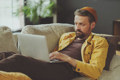 Young man using mobile phone while sitting on sofa at home