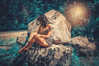 Young woman sitting on rock in forest