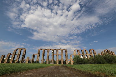 Wide angle of old ruin, roman aqueduct on field against blue sky with white clouds