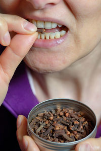 Close-up midsection of mature woman eating cloves in container