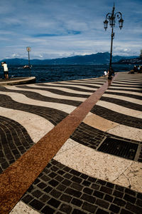 Striped pedestrian zone by sea against cloudy sky