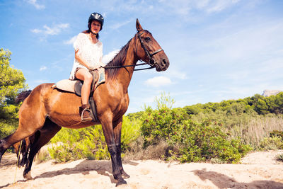 Woman riding horse on field against sky