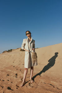 Portrait of young woman standing at beach against clear sky