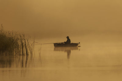 Silhouette man in boat on lake against sky during sunrise