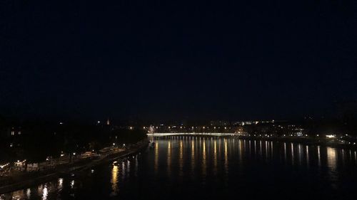 Illuminated buildings by river against sky at night