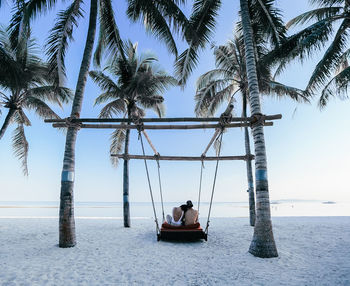 Man sitting on deck chairs at beach against sky