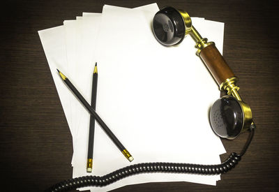 Close-up of telephone receiver and pencils over paper on table