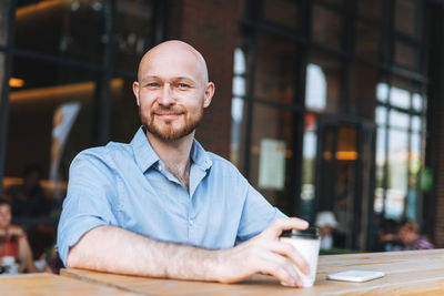 Adult attractive man forty years with beard in blue shirt businessman with cup of coffee at cafe