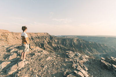 Full length of woman standing on rocky mountain against sky