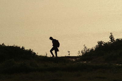 Silhouette man with umbrella walking on road against sky